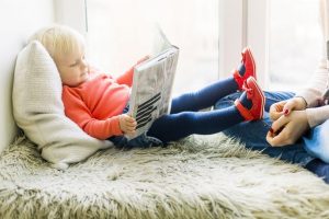 toddler girl reading with her feet propped up on mom